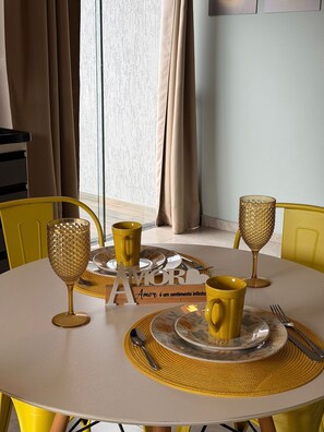 Un tavolo da pranzo rotondo con sedie gialle, un bicchiere decorato con motivi dorati, una tazza gialla e un altro bicchiere con decorazioni dorate su un sottopiattino.
