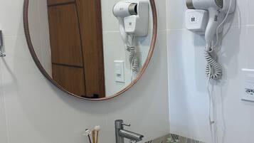 Ein Badezimmer mit einem rechteckigen Waschbecken, einem runden Spiegel und zwei an der Wand befestigten Haartrocknern.