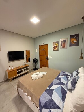 Una camera da letto con un letto, una televisione, una cassettiera in legno, una porta e decorazioni alle pareti.