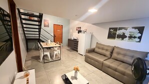 Un salon moderne comprenant un canapé, une table basse, une table à manger avec des chaises, un escalier et un coin cuisine.