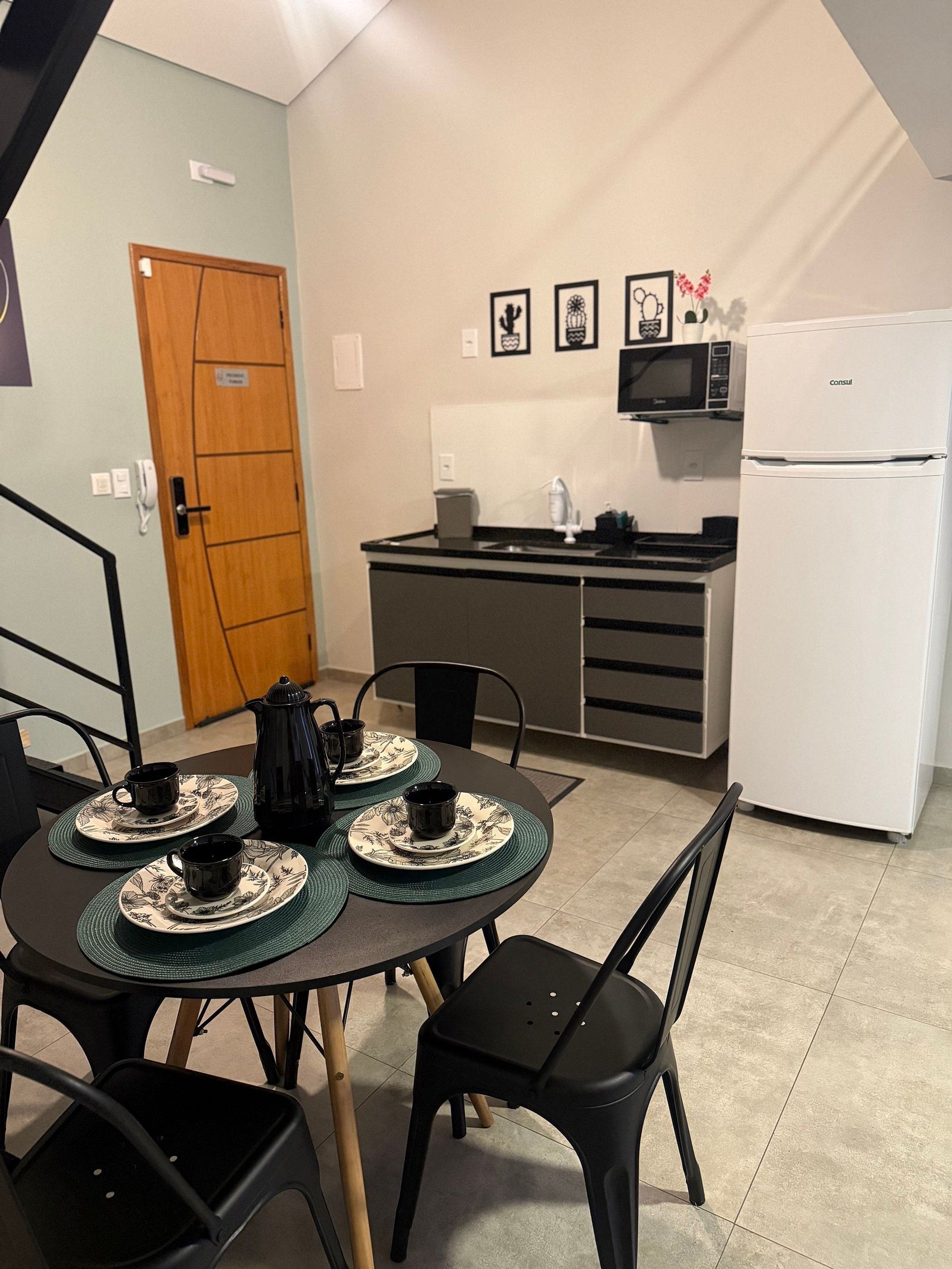 Cocina compacta con refrigerador, microondas y un pequeño comedor con mesa para dos.