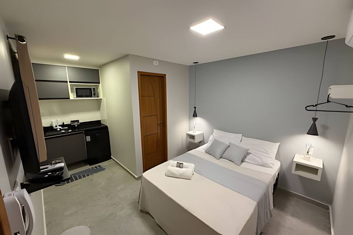 Habitación de hotel con cama, mesita de noche, lámpara y vista al área de la cocina.