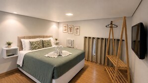 Une chambre moderne avec un lit, des tables de chevet, un porte-vêtements en bois suspendu et un téléviseur fixé au mur.