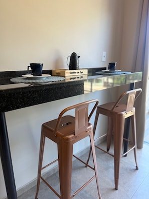 A kitchen area with a coffee maker, two chairs, and a wooden box labeled 'Cafettina de Caffe'. - Loft do Braga (Cabo Frio)