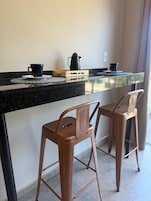 A kitchen area with a coffee maker, two chairs, and a wooden box labeled 'Cafettina de Caffe'.