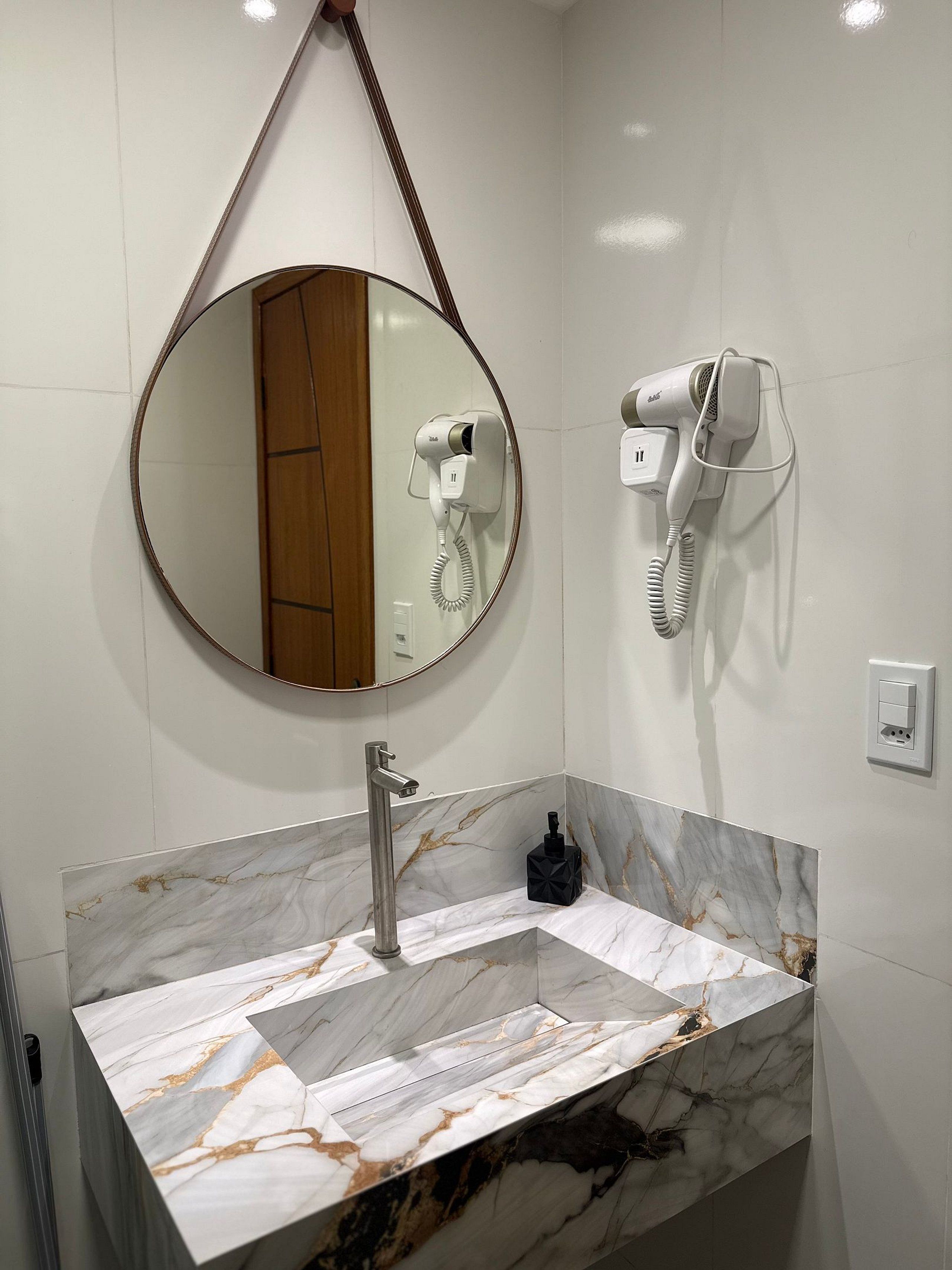 A bathroom with a marble vanity, a round mirror, a hairdryer, and a towel rack.