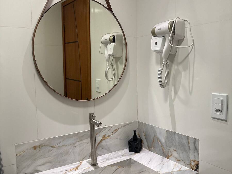 A bathroom with a marble vanity, a round mirror, a hairdryer, and a towel rack.