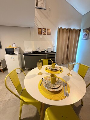 A dining area with a round table, yellow chairs, and a kitchen in the background. - Loft do Braga (Cabo Frio)
