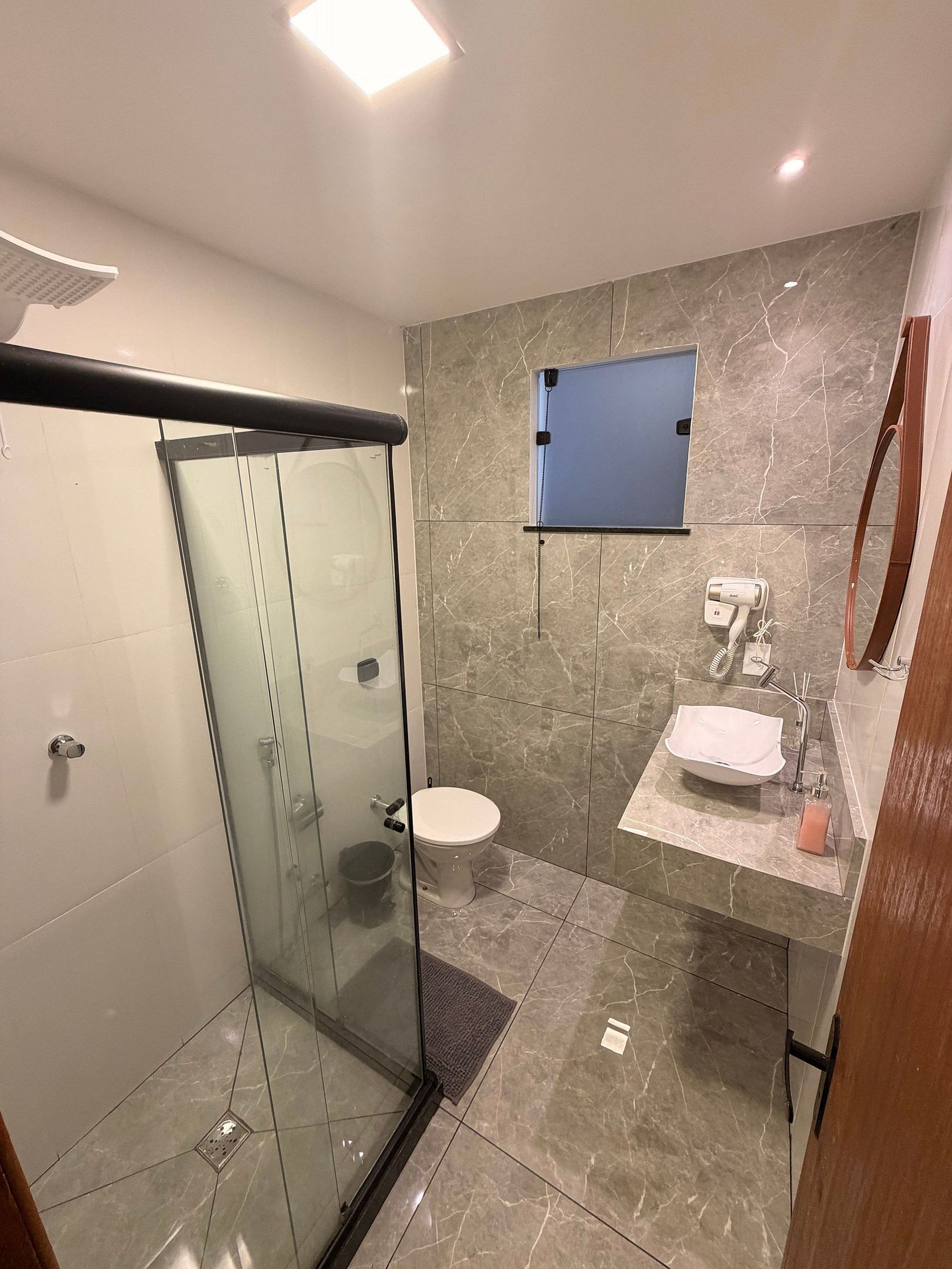 A modern bathroom with a glass-enclosed shower, a toilet, a sink with a marble countertop, and a mirror.