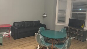 A living room with a black sofa, a red table, a teal dining table with chairs, a floor lamp, and a TV on a stand. - 1st fl 2-bedroom apartment with WiFi, AC in fantastic Philadelphia (Philadelphia)