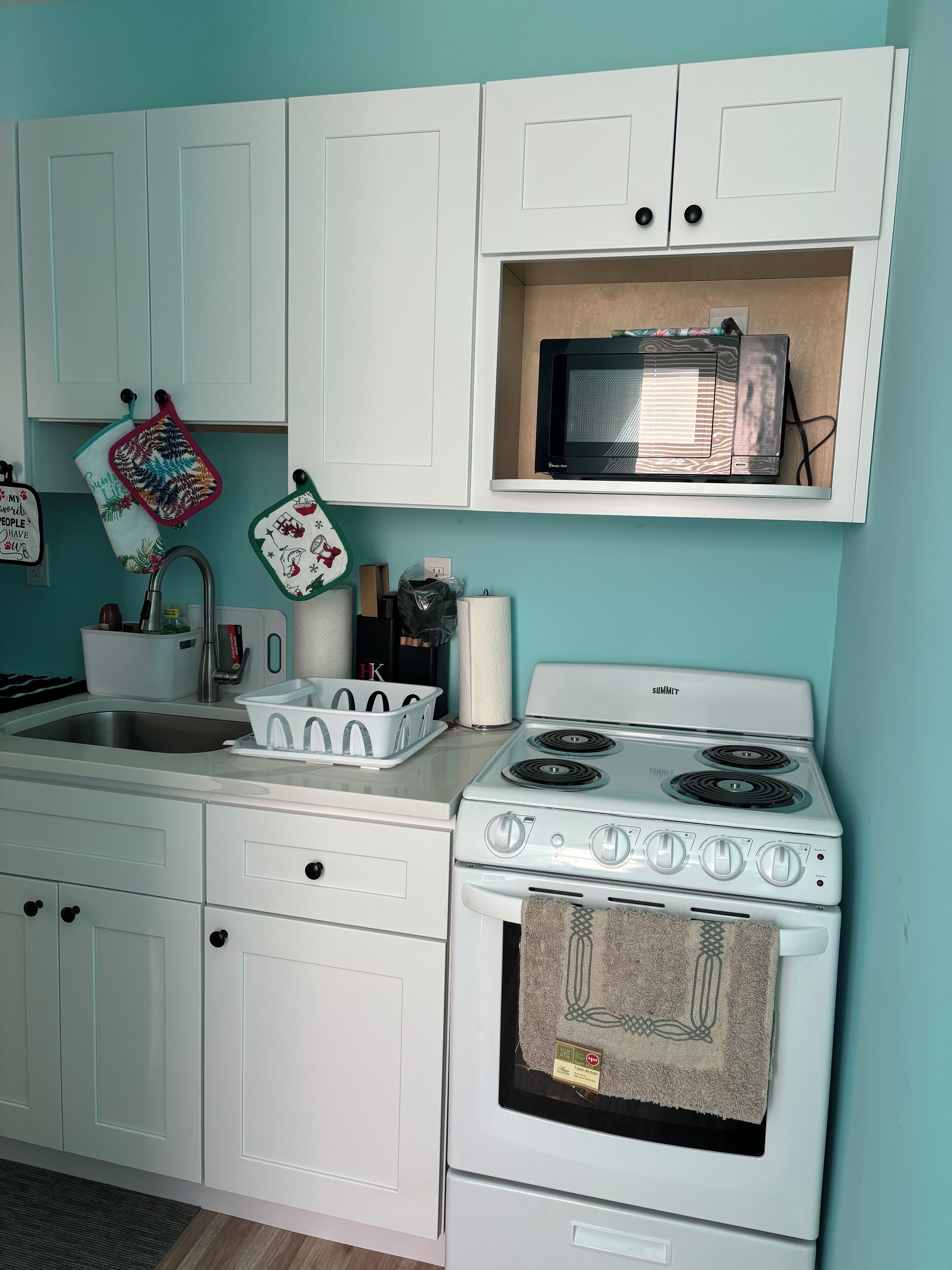 Une cuisine avec des meubles blancs, un four à micro-ondes, une cuisinière et un évier.