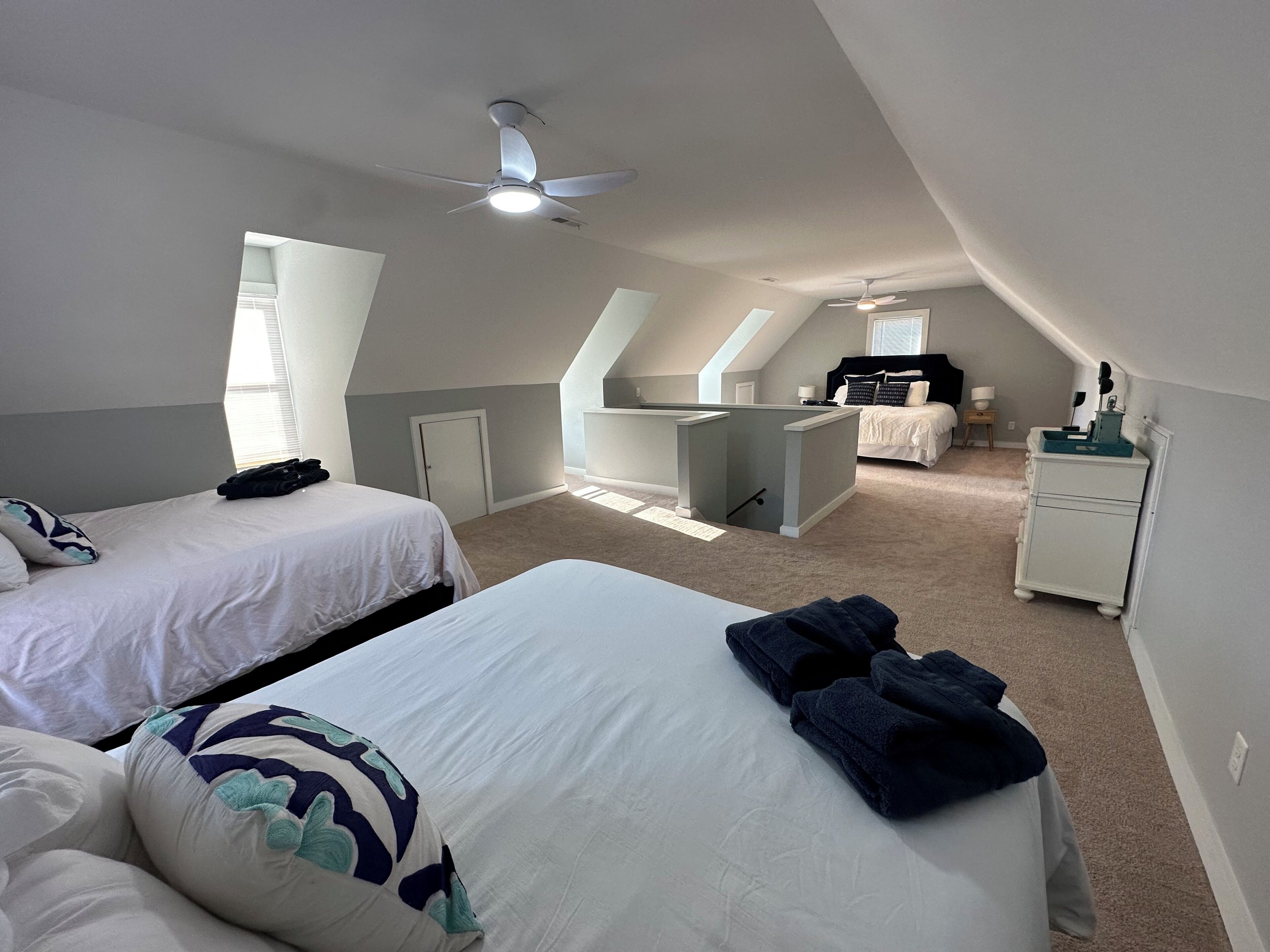 A spacious attic bedroom with two beds, a desk, and a ceiling fan.