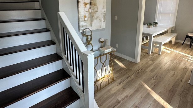 A staircase with dark wooden steps and white railings, leading to a room with a light wood floor, a white console table, and a large abstract painting on the wall. - Mini gold and pool spacious 3 level floor home for 14 people  (Raleigh)