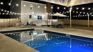 A swimming pool with string lights, a covered patio, and a house in the background. - Mini gold and pool spacious 3 level floor home for 14 people  (Raleigh)