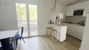 Une cuisine moderne avec des meubles blancs, un îlot central doté de tabourets, une table à manger avec des chaises et une grande porte-fenêtre coulissante donnant sur un espace extérieur.