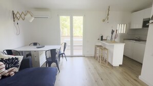 Un espace de vie et de salle à manger moderne, à aire ouverte, comprenant une cuisine, une table à manger avec des chaises, un canapé et une porte-fenêtre coulissante donnant sur un balcon extérieur.
