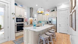 A modern kitchen with white cabinetry, a central island with bar stools, stainless steel appliances, and pendant lighting. - Playful & Fun at Coco's~ Golf Cart, Bikes, 2 Pools PLUS Easy beach access (Inlet Beach)