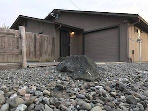 A building with a garage door, a wooden fence, and a large rock in the foreground. - Quiet 2BR • Garage • Yard • EV Charger – Eureka (Eureka)