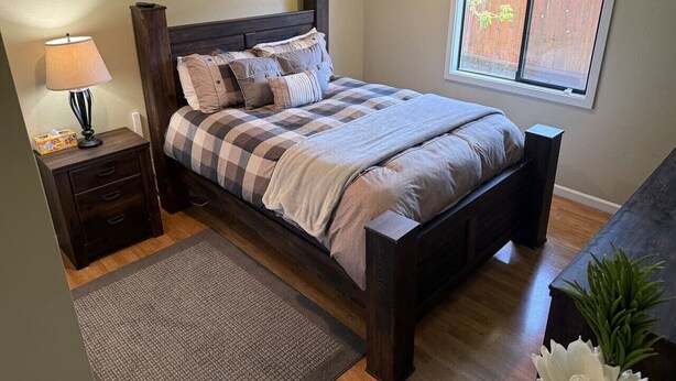 A bedroom with a bed, nightstand, lamp, and window.