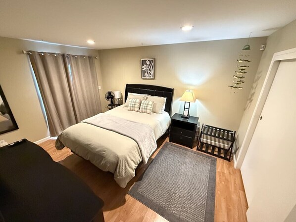 A bedroom with a bed, bedside tables, a desk, a chair, a rug, curtains, and a wall-mounted shelf.