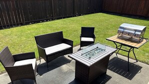 An outdoor patio with wicker furniture, a glass-top table, and a barbecue grill.