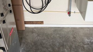 A utility room with a control panel, a white device with a green light, and a water pipe system.