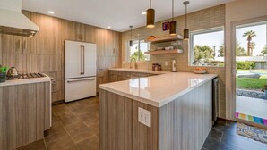 Een moderne keuken met een centraal eiland, houten kastjes en hangende lampen.