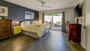 Une chambre à coucher comprenant un lit, une commode, un téléviseur et une porte-fenêtre coulissante donnant sur un espace extérieur.