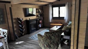 A cozy living room with a fireplace, a television, and a bookshelf. - Riverside cabin in the woods (Bracebridge)