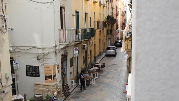 A narrow street with buildings, outdoor seating, and a parked car. - Centromare Trapani (Trapani)