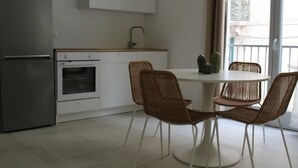 A kitchen with a refrigerator, oven, and white cabinets. There is a round table with four wicker chairs and a window with a view of the outside. - Centromare Trapani (Trapani)