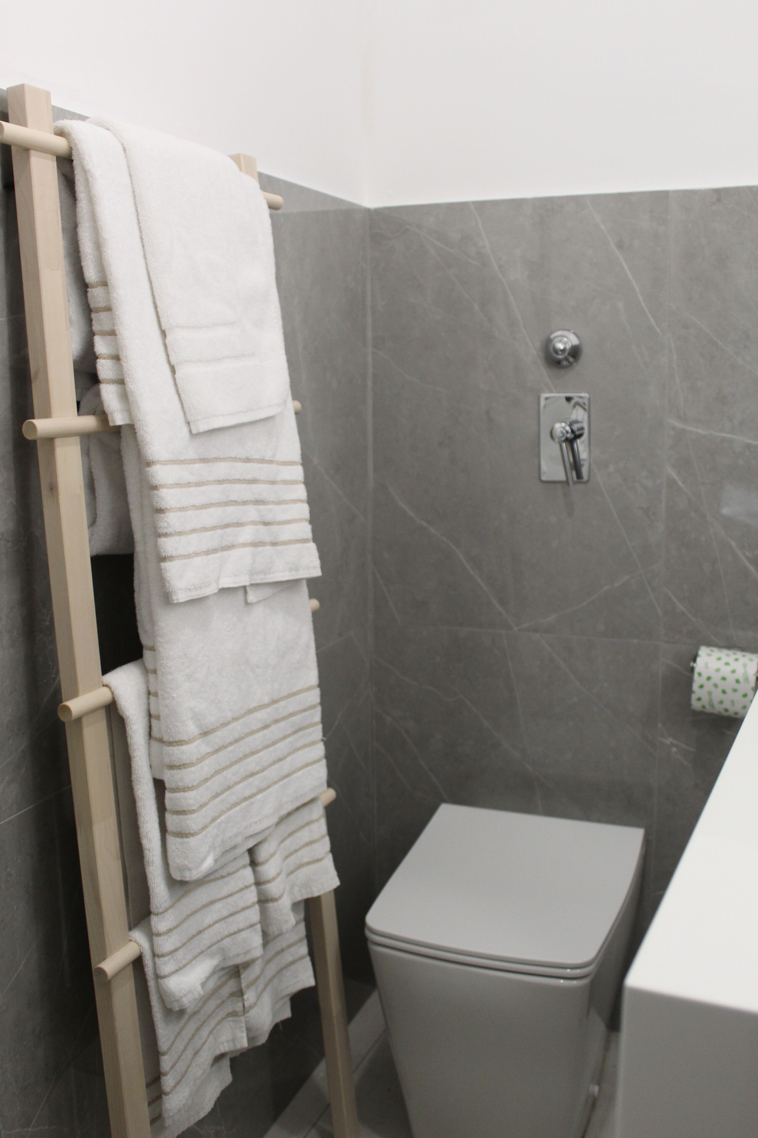 A bathroom with a towel rack holding multiple towels, a toilet, and a showerhead on the wall.
