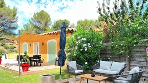 An outdoor patio with a wooden deck, wicker furniture, and a small table. - La Maisonette Provençale (Ventabren)