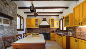 A kitchen with yellow cabinets, a stone wall, and a wooden dining table. - Villa Vicanti: Private Paradise (Mesochori)