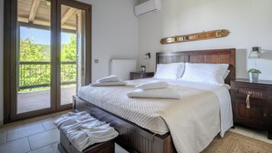 A bedroom with a large bed, a wooden headboard, a nightstand, a lamp, and a view of the outdoors through a sliding door. - Villa Vicanti: Private Paradise (Mesochori)