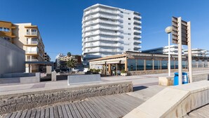 Uma orla urbana moderna com um edifício de vários andares, uma área de estar coberta ao ar livre e um calçadão.
