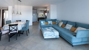 Uma sala de estar moderna com um sofá azul, uma mesa de jantar com cadeiras e luminárias pendentes.