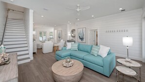 A spacious living room with a teal sofa, a round coffee table, and a staircase. - NEW - Symphony! Sleeps 18! Pool! Golf Cart (Santa Rosa Beach)