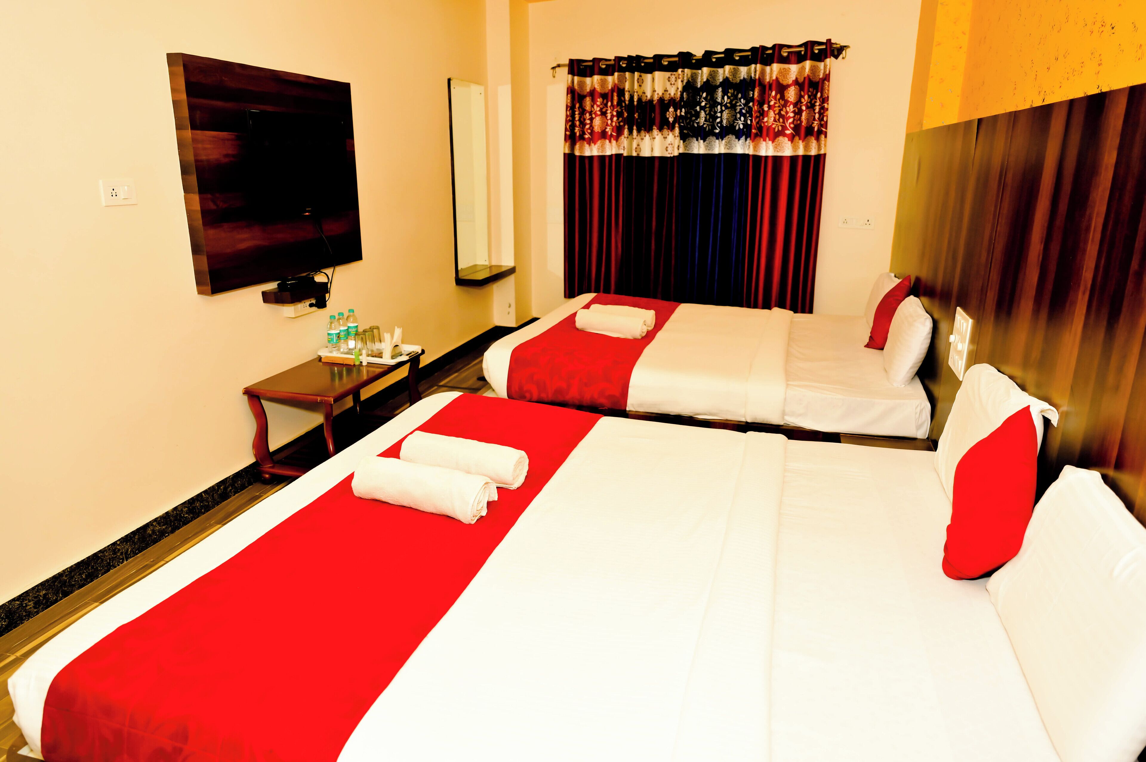 Quarto de hotel com duas camas, televisão, espelho e uma mesinha de apoio com produtos de higiene pessoal.