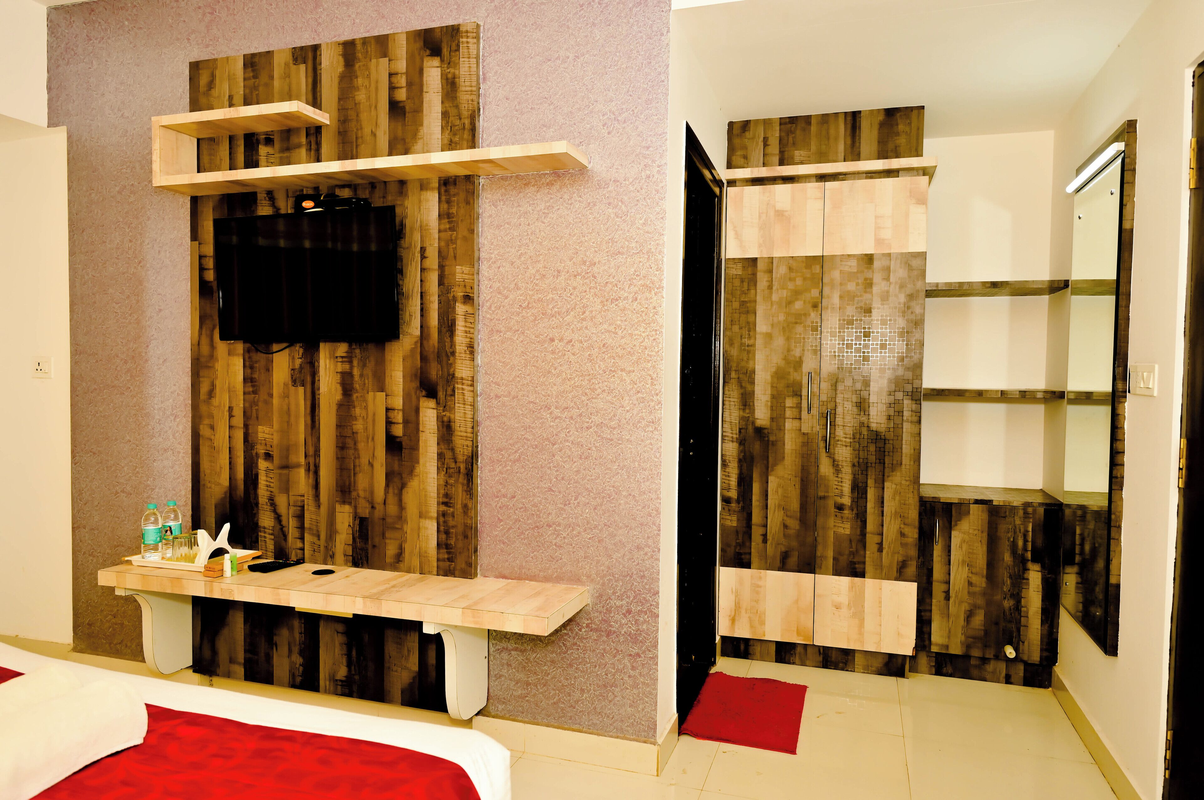 A hotel room with a wooden wall, a flat-screen TV, a wooden bench, and a bed with a red blanket.
