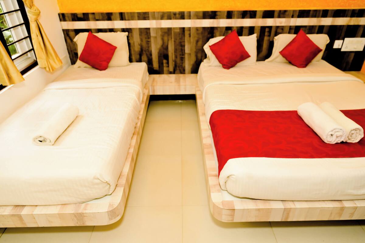 Two single beds with wooden headboards, red and white bedding, and a yellow wall with a window and curtain.