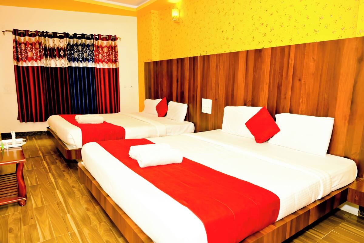 A hotel room with two beds, wooden headboard, red and white bedding, wooden flooring, and a curtain with a red and white pattern.