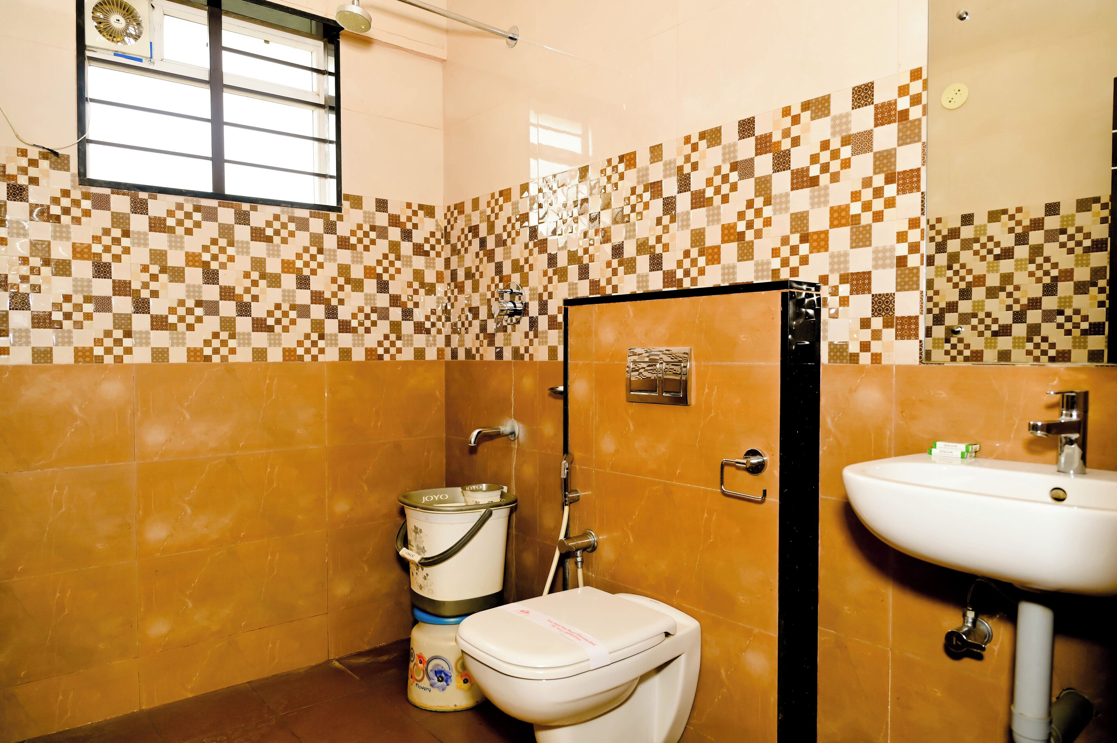 Un baño con pared de azulejos, inodoro, lavamanos y ventana.