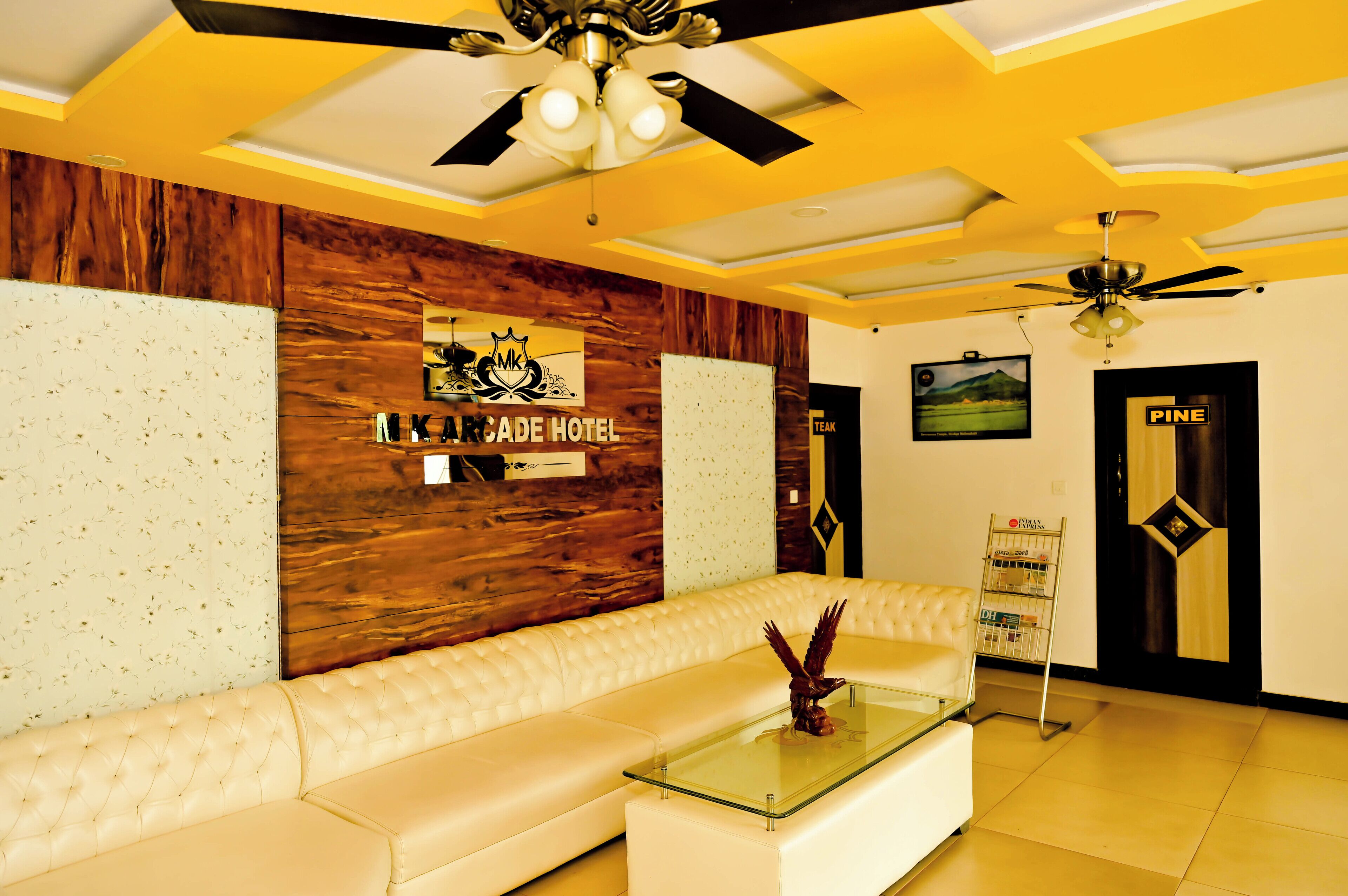 A hotel lobby with a wooden accent wall, a white leather sofa, a glass coffee table, and a ceiling fan.