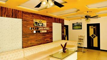 A hotel lobby with a wooden accent wall, a white leather sofa, a glass coffee table, and a ceiling fan.
