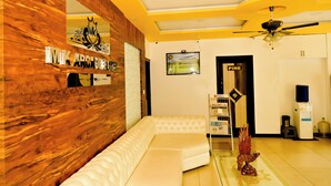 Un salon moderne avec un mur d’accent en bois, un canapé d’angle blanc, un ventilateur de plafond et une petite étagère remplie de livres.