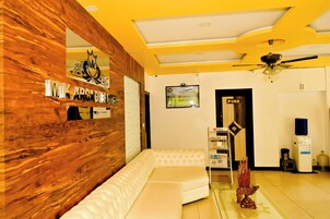 Una sala moderna con una pared de acento de madera, un sofá seccional blanco, un ventilador de techo y una pequeña estantería con libros.