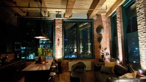 Een modern interieur met zichtbare houten balken, grote ramen met uitzicht op de stad, een bar en een gezellige zithoek.