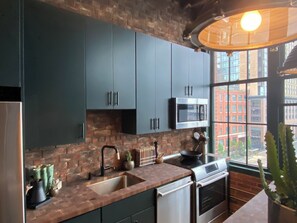 A modern kitchen with dark cabinets, a microwave, a stove, and a sink. - Fort Point Corner of Windows brick & beam loft (Boston)