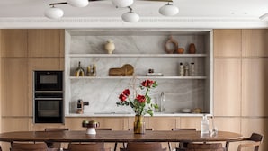 Una cocina moderna con armarios de madera, salpicadero de mármol y un comedor con mesa y sillas de madera.